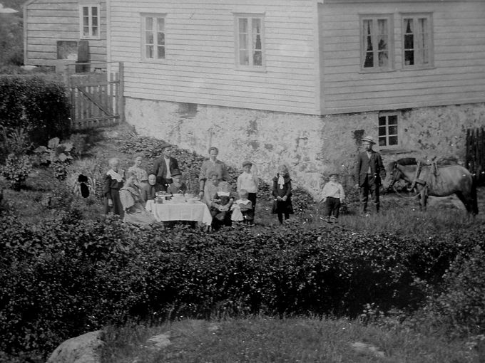 Billede tatt 1906 av hageselskap i Garen. Stående fra høyre: Peder Andreas, Ludvik, Helene, Alfred og Helga, med dukke. Stående helt til venstre: Maren Serine. Sittende ved bordet, midt imot: Inga og Amund Amundsen. Sittende til høyre: Anna Tobine med Arne på fanget. De øvrige ikke identifisert.